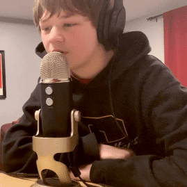 Young Caucasian boy wearing a black hoodie speaks into a microphone
