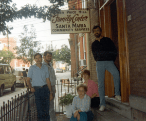 two men standing, two women sitting and one man with a beard and moustache stands in the doorway of the Lower Price Hill Family Center at Santa Maria Community Services